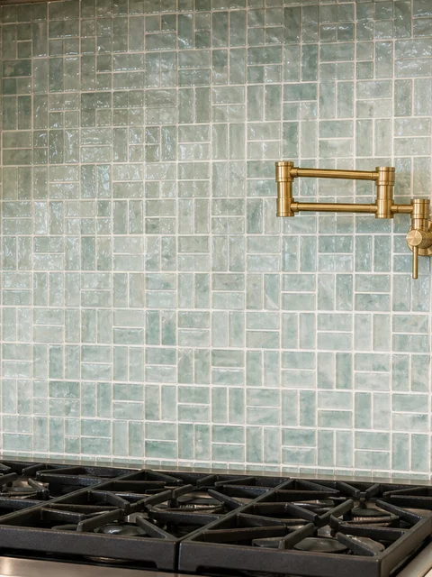 Sea-green glazed tile backsplash with a brass pot filler over the range
