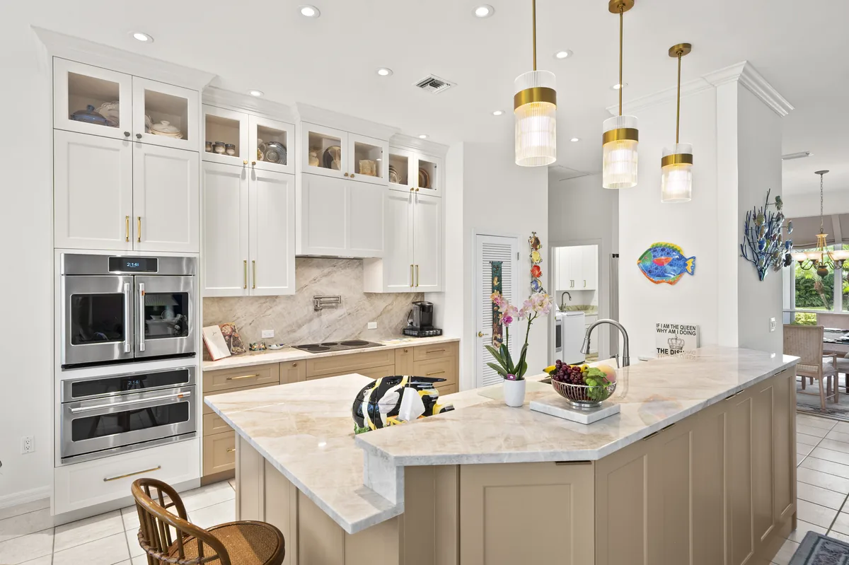 Completed white kitchen with a large island, brass pendant lights, and warm wood flooring