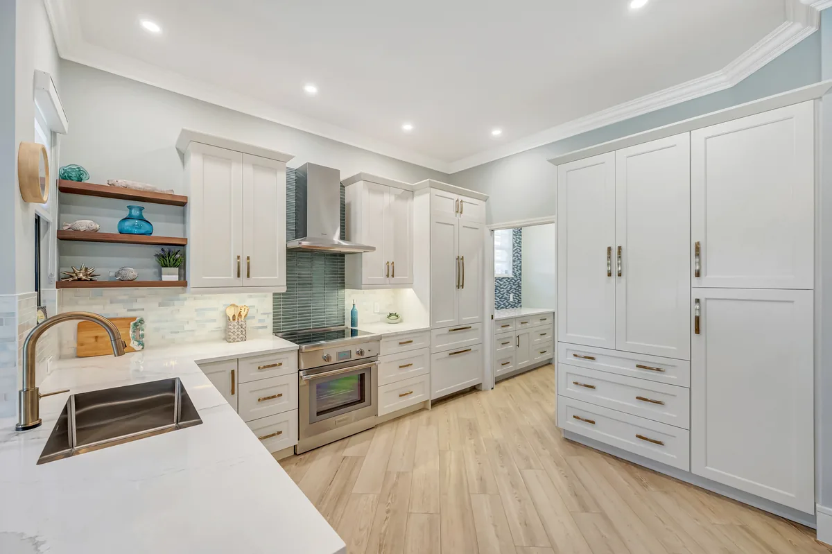 Completed bright kitchen with white cabinetry, pale wood flooring, and sea-glass tile details